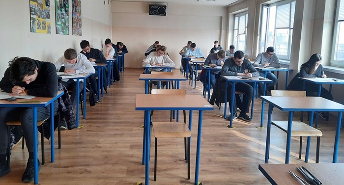 Uczniowie siedzą przy stolikach i piszą na kartkach